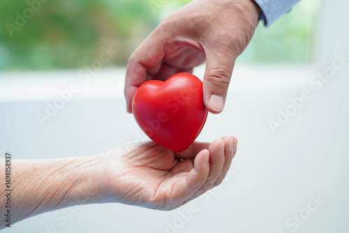 Asian elder senior woman patient holding red heart in hospital.