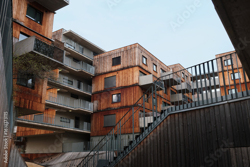 Modern multi-story apartment building in Vienna featuring protruding concrete Bauhaus-style balconies, wooden brown facade panels, under a gray sky.