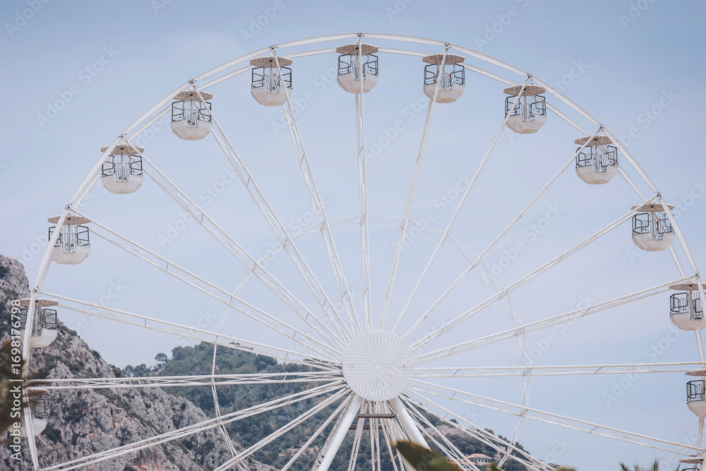 Fototapeta premium Majestic ferris wheel gracing the skyline against a backdrop of serene mountains and a clear blue sky during a sunny afternoon