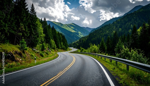 Fototapeta Naklejka Na Ścianę i Meble -  A winding road carves through a lush, mountainous landscape under a partly cloudy sky. Green trees line the roadside