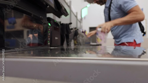 Man Puts Groceries Into Bags at Self-checkout Counter in Store. Shopping for Groceries at Supermarket. Man operates Self-service Checkout, Scanning His Items and Placing Them in Bags.