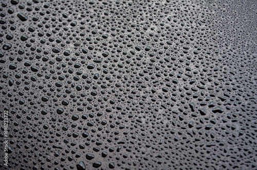 Closeup of black surface with dense water droplets forming textured condensation background.