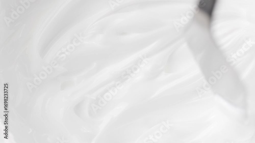 Top-down view of metal spatula smearing white cream. Rotating texture of facial or body cosmetic mask. Perfect for skincare and beauty content.
