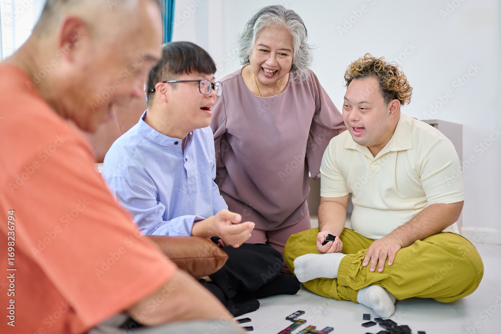 Obraz premium A grandmother and grandfather are playing dominoes together with a man with Down syndrome at home