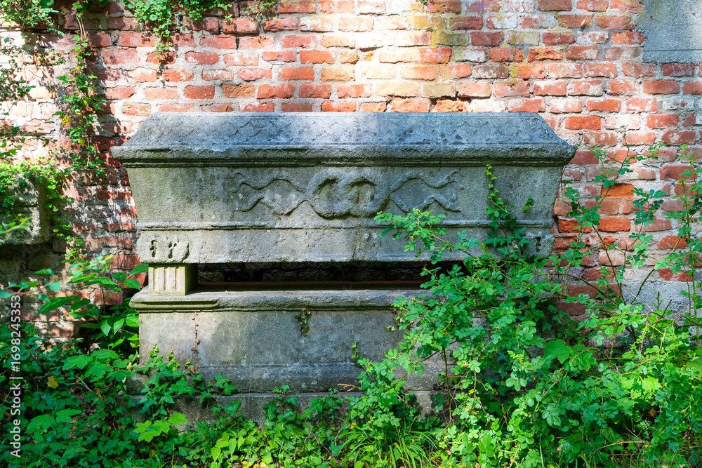 Fototapeta premium sehr alte Grabstätte in Form eines Sarges vor eine Ziegelmauer Alter Südfriedhof München