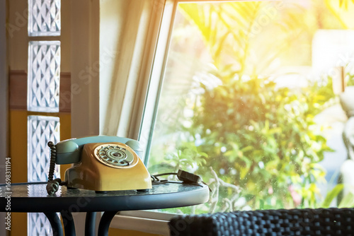 Classic rotary telephone or dial telephone stands on table by window in home. Old retro rotary dial telephone. Classic communication device with coiled cord. History of communication device concept.