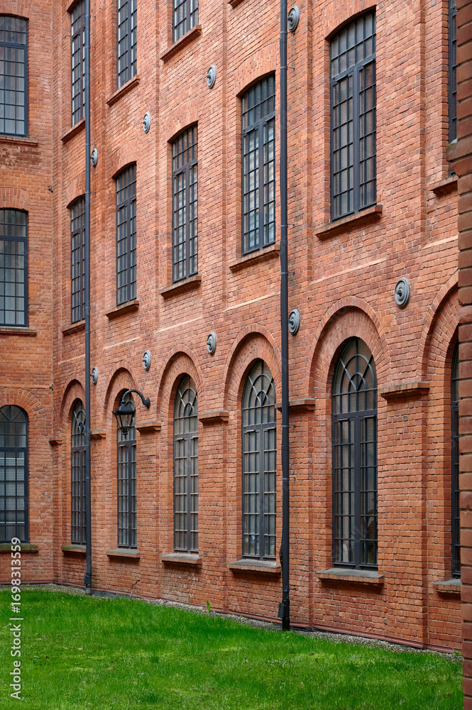 Fototapeta premium A close-up of an intricately designed brick building facade with arched windows, featuring metal outdoor stairs and black wrought iron lamps, showcasing the fusion of form and function in Łódź