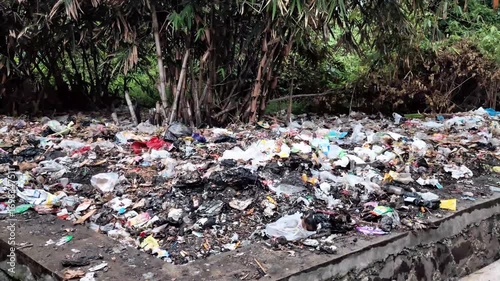 Pile of mixed plastic waste, food wrappers, and household garbage dumped in an open area near a drainage channel, showing environmental pollution and improper waste management.