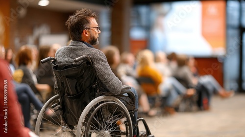 A man in a wheelchair listens attentively to a presentation in a conference setting, showcasing inclusivity and engagement in the audience.