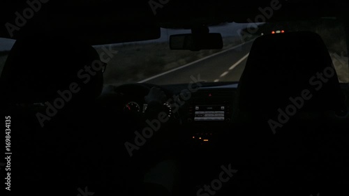A dimly lit car interior with a driver steering through a deserted night road. The vehicle's dashboard glows with light, creating a sense of solitude, focus, and night travel.