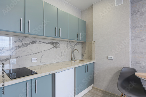 modern kitchen with blue cabinets, marble backsplash, and countertops. Appliances are sleek and silver hardware adds a contemporary touch