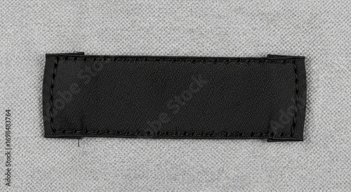 Blank black fabric label stitched onto a textured grey non-woven textile background, offering copy space for branding or text.