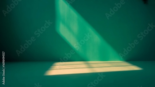 A bright beam of light from a window shines on a teal wall and floor. The resulting contrast creates an interesting interplay of light and shadow.