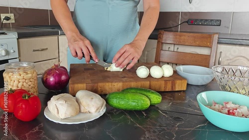 Making a salad at home. A girl cuts boiled chicken eggs with a knife on a wooden cutting board. There are cucumbers, beans and boiled chicken breast on the table