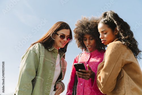A group of three female friends standing and looking at a phone that one of them is holding while one of them is smiling
