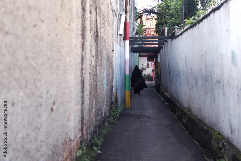 Obraz premium narrow alley with a woman wearing a black hijab walking away