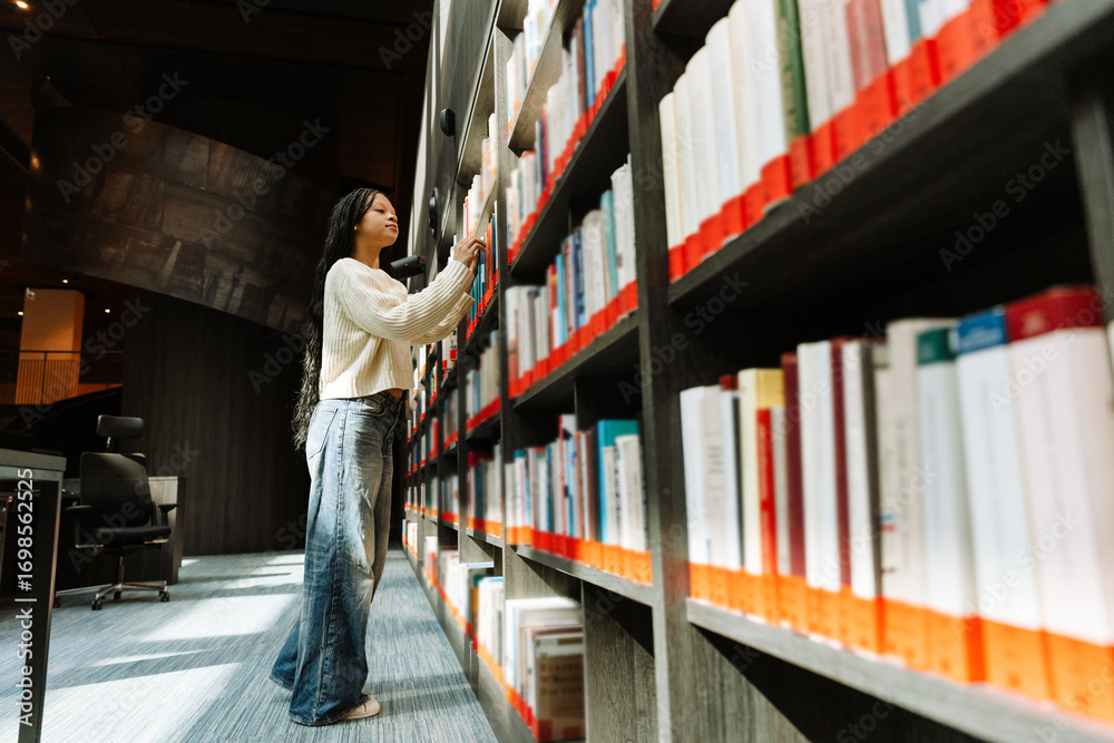 Obraz premium A female student chooses a book on a bookshelf