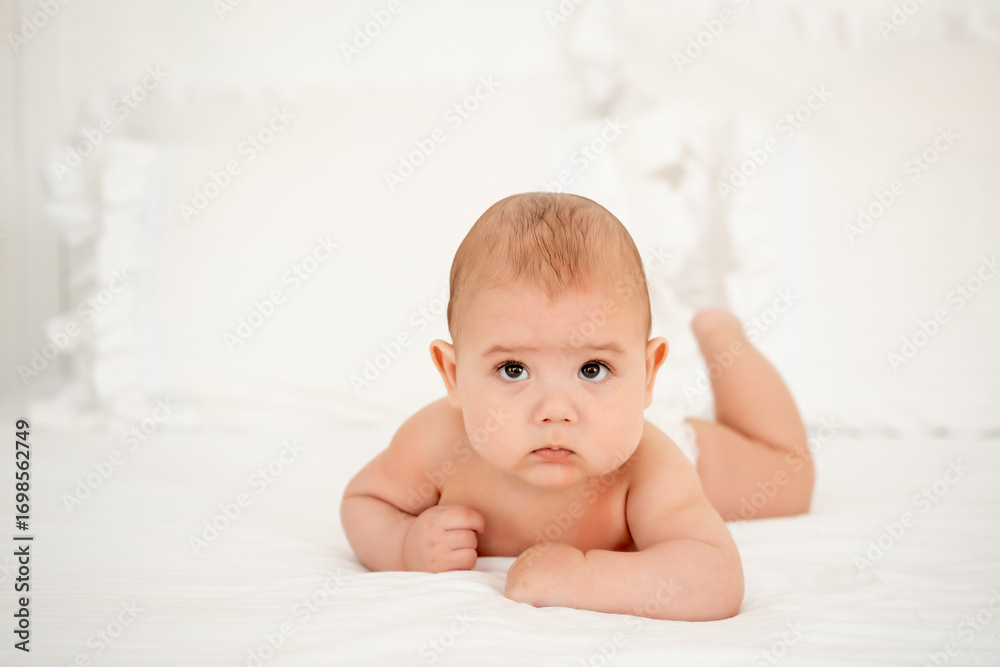 A baby boy in diapers on a white bed in a bedroom, a cute little baby of six months, a place for text A baby boy in diapers on a white bed in a bedroom, a cute little baby of six months, a place for text