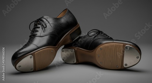 Elegant black leather tap shoes, poised for a rhythmic performance on a sleek gray surface
