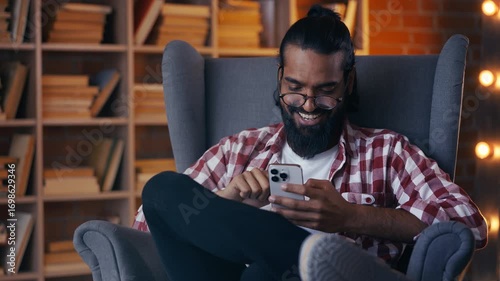 Smiling Indian student scrolling social media in library, using dating app