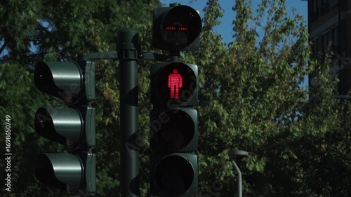 Red pedestrian signal shows a walking man, indicating stop for pedestrians. A red silhouette of a walking person illuminated on a pedestrian traffic light, signaling to halt crossing the street