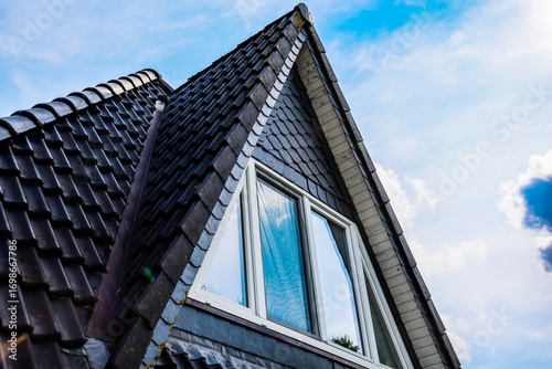 Modern triangular roof with black tiles and white window reflecting blue sky