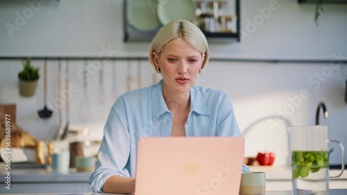 Focused blonde typing laptop at kitchen closeup. Satisfied lady closing computer
