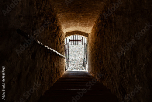Stone passage with stairs leading to bright iron gate