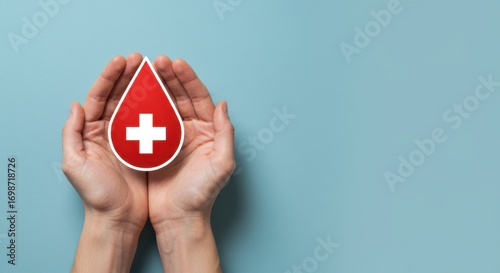 Hands holding a red blood drop with a white cross symbol, representing blood donation and healthcare awareness