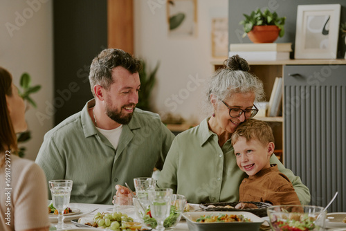 Foto Caucasian senior woman embracing smiling child while sitting at dining table wit