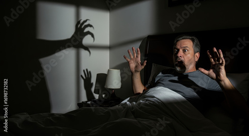 Nighttime scary stories unfold with frightening shadow monster looming over man in bed, creating fear. Nighttime scary stories show danger lurking in dark, frightening shadow that reaches,
