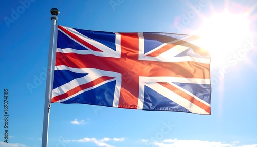 The Union Jack flag waving against a bright blue sky with the sun shining in the background.