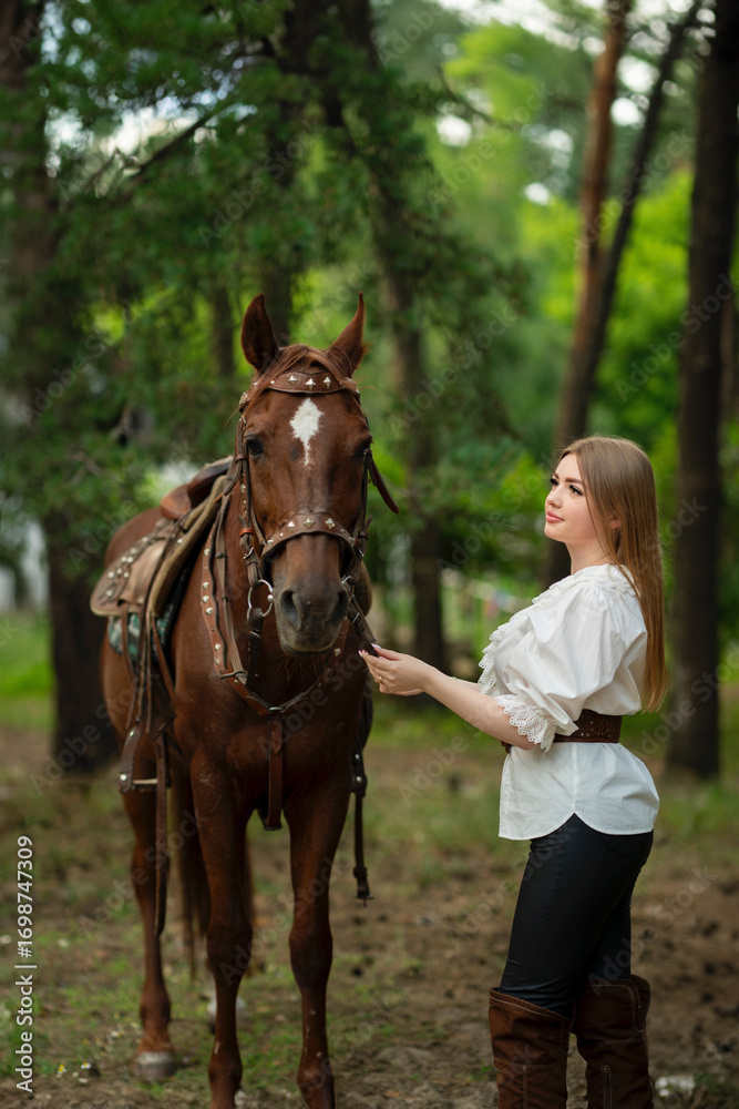 Obraz premium Beautiful young woman in stylish white blouse, black pants and high boots with a horse outdoors