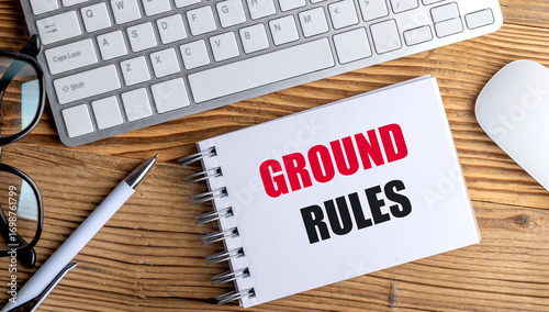 Notebook with the words ground rules on wooden desk with keyboard, pen, glasses and mouse