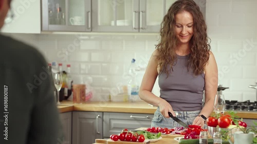 Mid adult couple preparing for cooking in modern kitchen at home, wearing casual cloth. Man and woman cleaning and slicing vegetables, fondling kitten.