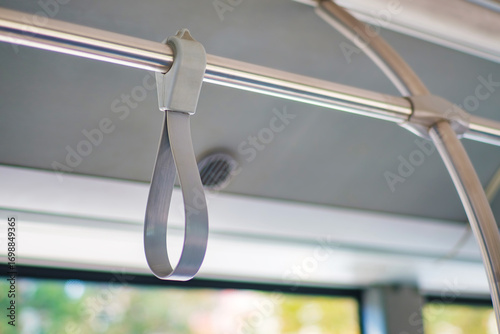 Close-up of a hand strap on public transportation, attached to a metal overhead bar. The grip provides stability for standing passengers. Designed for safety and commuter comfort. Selective focus.