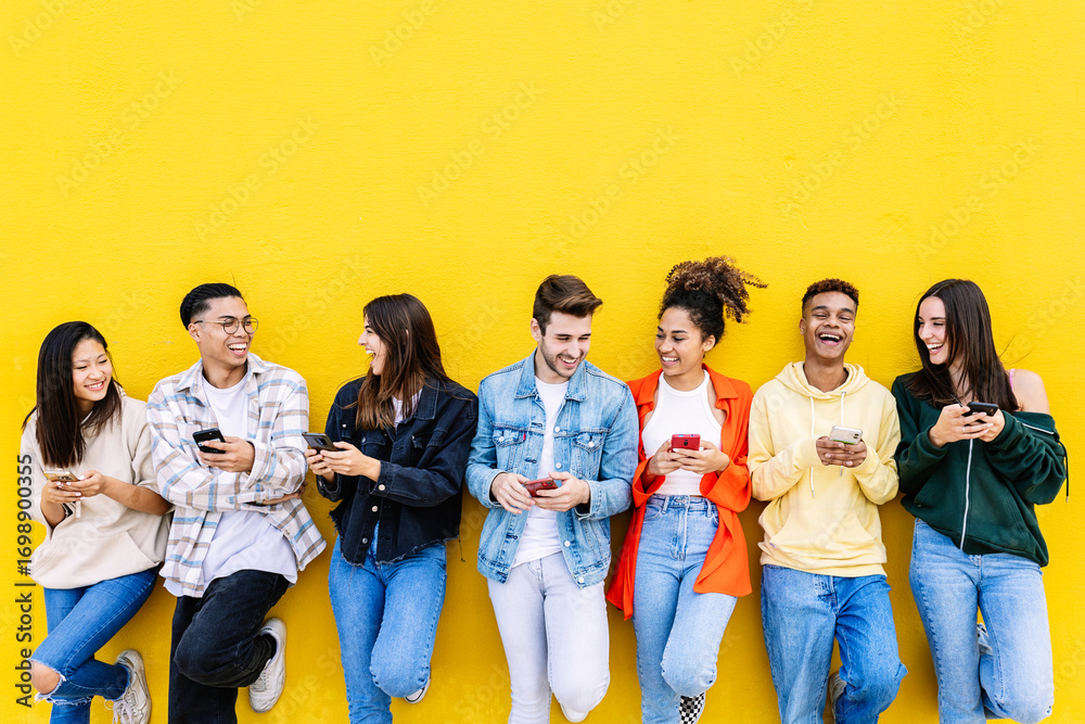 © Xavier Lorenzo - Young group of people having fun using mobile phone over yellow wall. Communication and social media concept