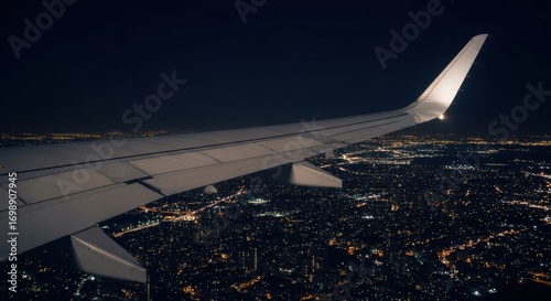 Airplane wing over city lights at night in illuminated urban landscape