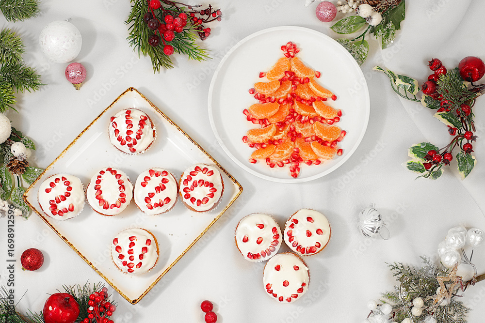 Obraz premium Christmas and New Year dishes. Curd muffins with pomegranates in glaze with numbers 2026 and a Christmas tree made of tangerines for a festive table, an idea for decorating food