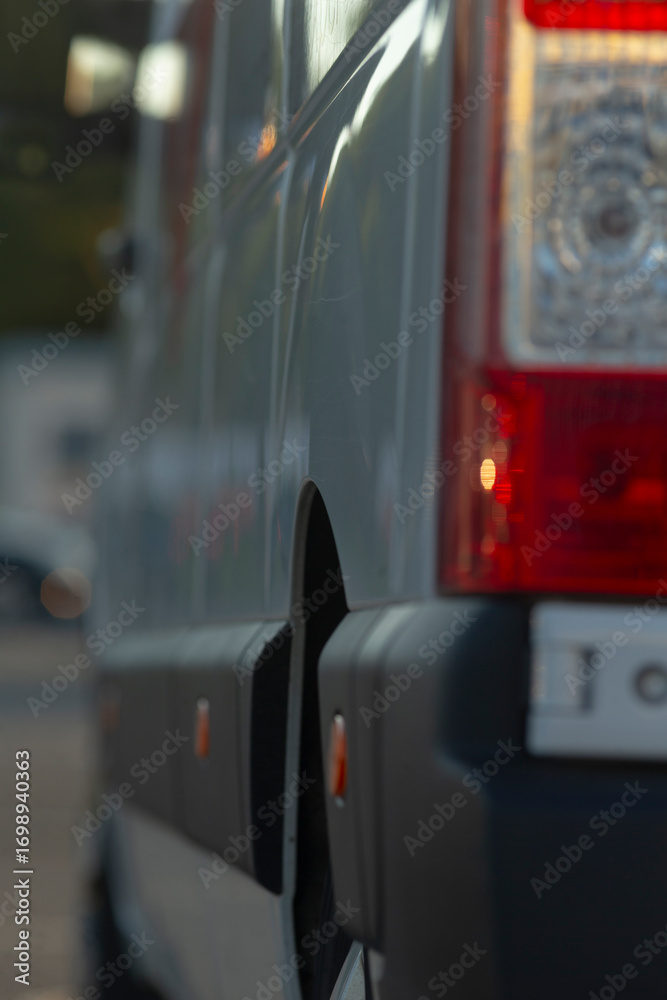 Fototapeta premium In the image, the focus is on the side of a van, showcasing the intricate design of its tail light and wheel well, while a softly blurred background creates an appealing artistic effect