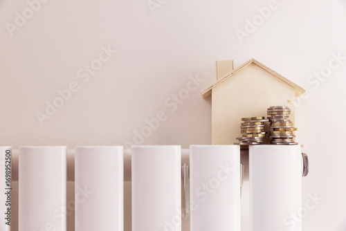 Household cost of living crisis. Money and a house model on a heating radiator