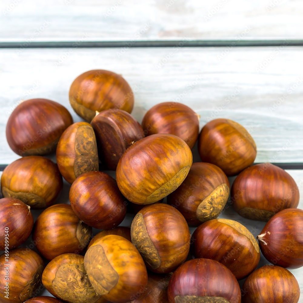 Obraz premium Pile of brown chestnuts on a light wooden surface