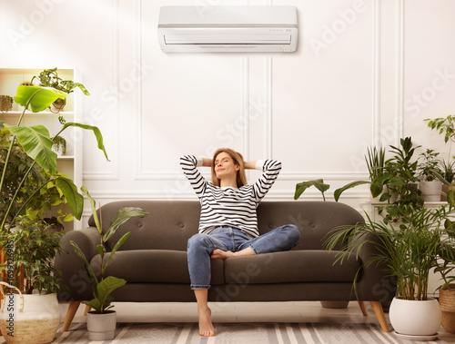 Billede på lærred Woman relaxing on sofa surrounded by potted houseplants at home