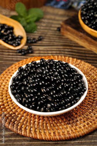 Black beans in bowl on bamboo mat with wooden spoons - healthy legumes and grains for cooking