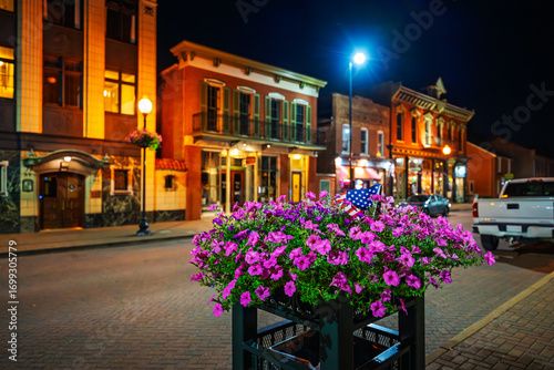 Fototapeta Naklejka Na Ścianę i Meble -  A flower basket full of pink petunias with a small American flag on the brick paved streets of the illuminated small town of historic Saint Charles, Missouri, USA.