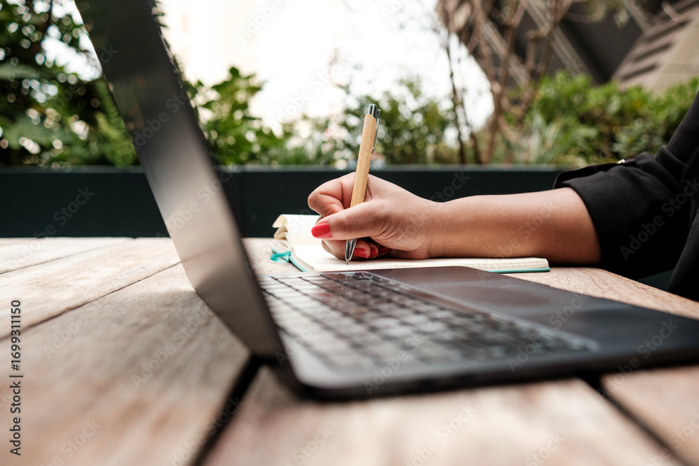 Fototapeta premium Businesswoman writing notes while working remotely outdoors