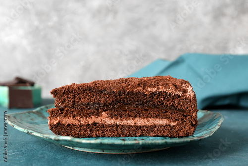 Foto Plate with piece of tasty chocolate cake on blue table in kitchen, closeup