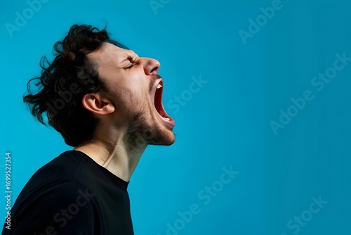 Side view, profile photo of a man shouting with his mouth wide open, isolated on a blue background. Concept with copy space.