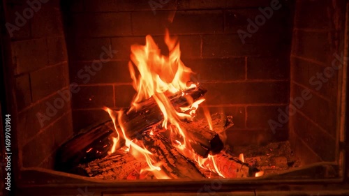 Home cozy brick fireplace with red flame and firewood. 4K endless video footage 