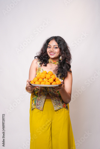 Happy young indian woman holding plate of bundi laddu or ladoo sweets celebrating diwali festival isolated on white background. Dessert sweet food or snack of india.